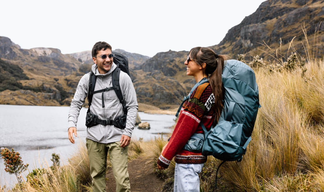 Hikers wearing Osprey backpacks on mountain trail beside lake landscape