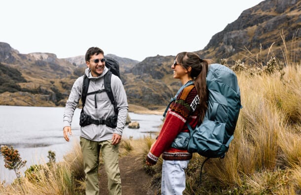 Hikers wearing Osprey backpacks on mountain trail beside lake landscape