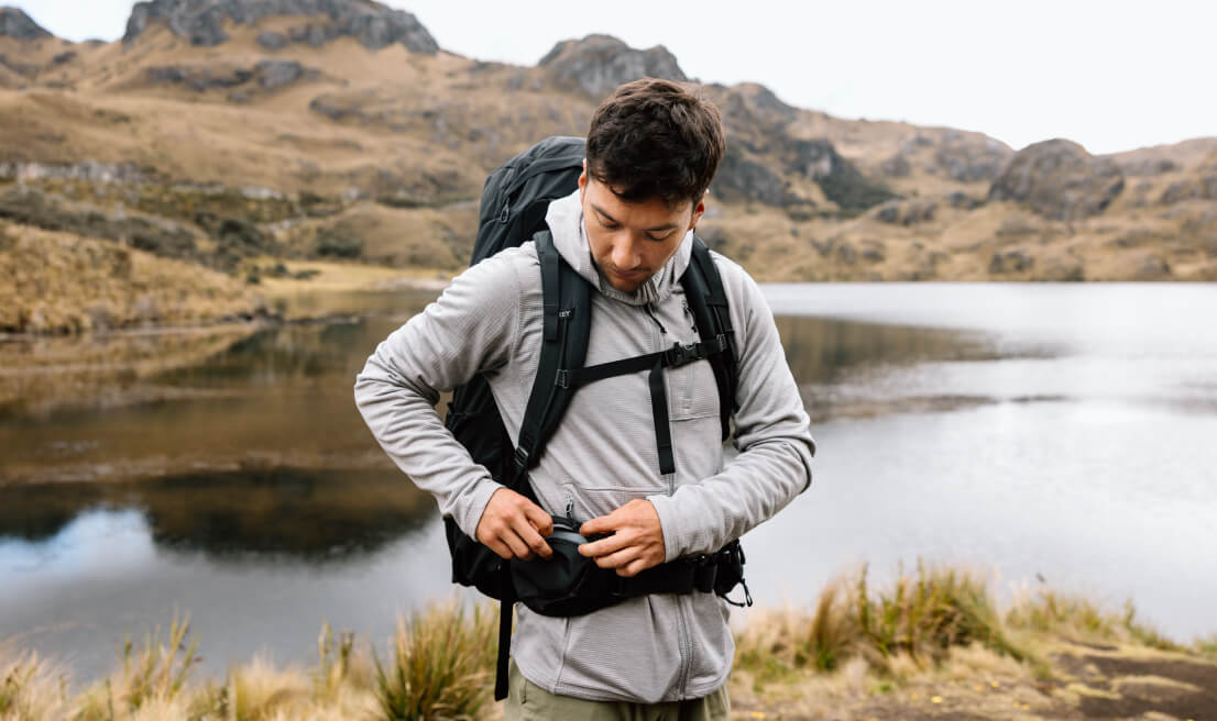 Traveler adjusting Osprey Farpoint Trek backpack by scenic mountain lake