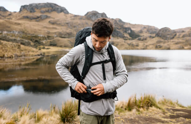 Traveler adjusting Osprey Farpoint Trek backpack by scenic mountain lake