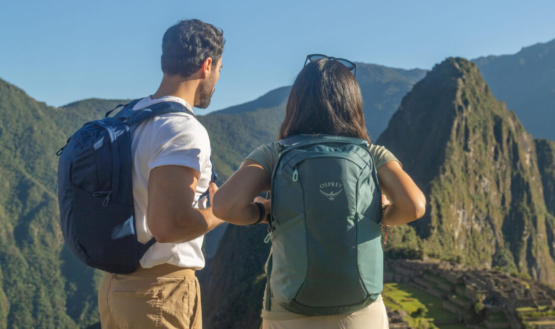 Travelers wearing Osprey Farpoint and Fairview daypacks overlooking mountain landscape