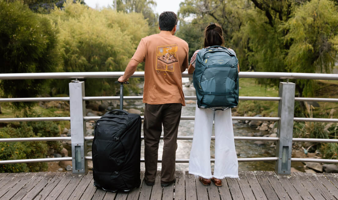 Two travelers with wheeled bag and Osprey Farpoint backpack overlooking riverside walkway