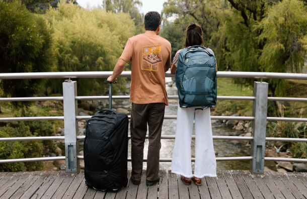 Two travelers with wheeled bag and Osprey Farpoint backpack overlooking riverside walkway