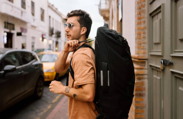 Traveler carrying Osprey Farpoint wheeled pack walking through city street
