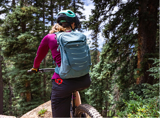 Mountain biker wearing an Osprey backpack riding through a forest trail.