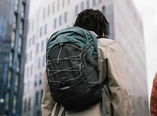 Person wearing an Osprey backpack standing in an urban area with tall buildings.