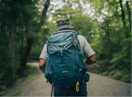 Hiker wearing an Osprey backpack walking through a forest trail.