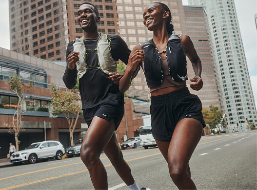 Two runners wearing Osprey running vests jogging through a city street.