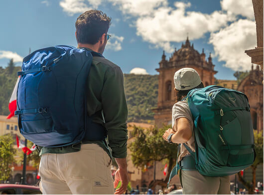 Travelers wearing Osprey backpacks exploring a historic city plaza with a cathedral in the background.