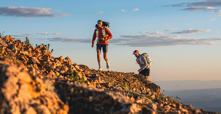 Two trail runners on a rocky mountain ridge at sunrise