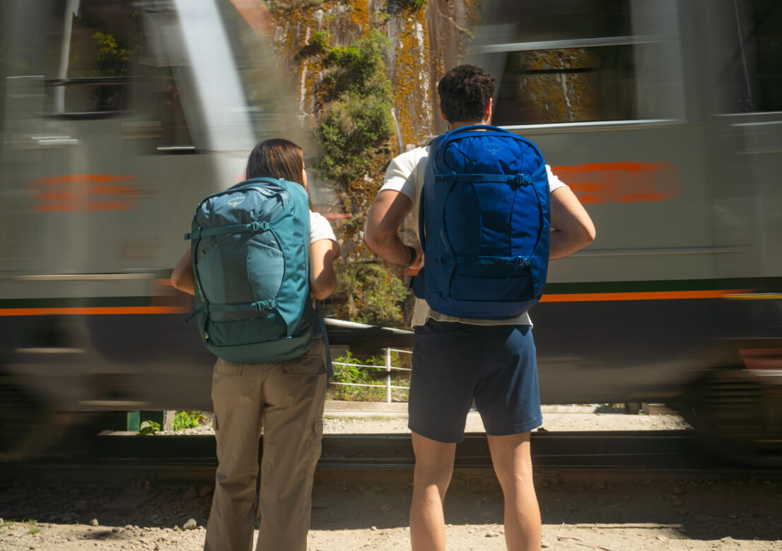 Travelers with Osprey backpacks waiting for train to pass.