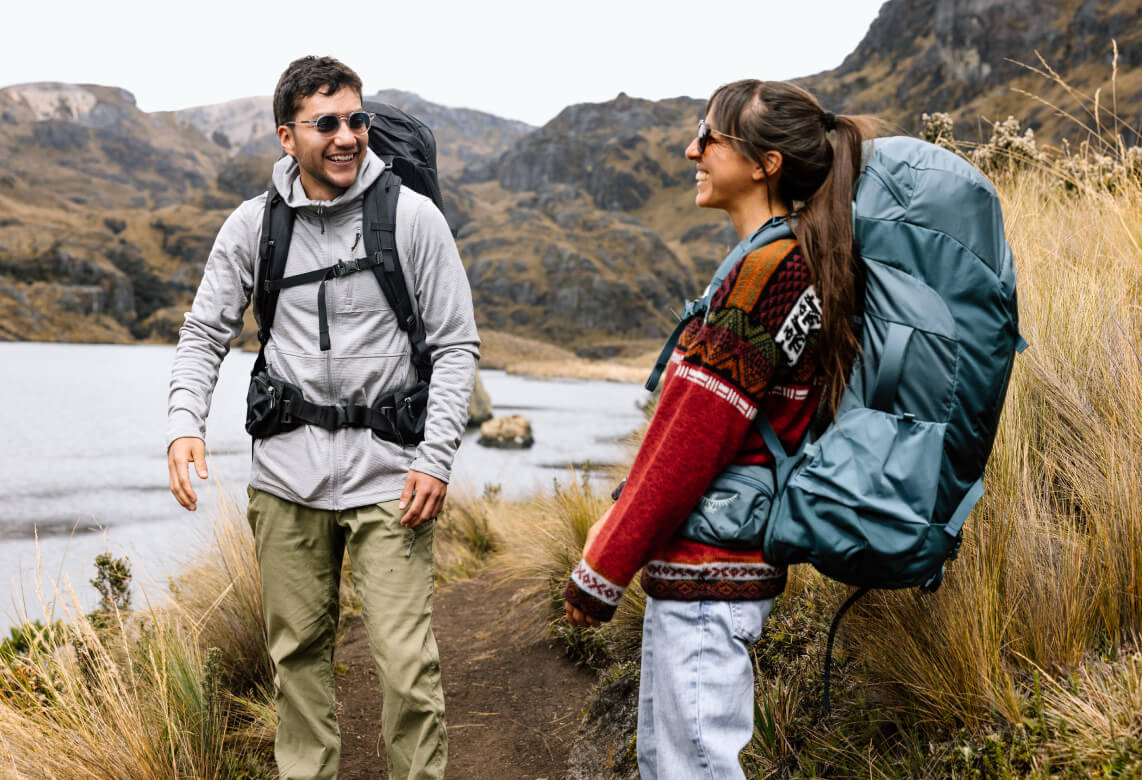 Hikers wearing Osprey backpacks on mountain trail beside lake landscape