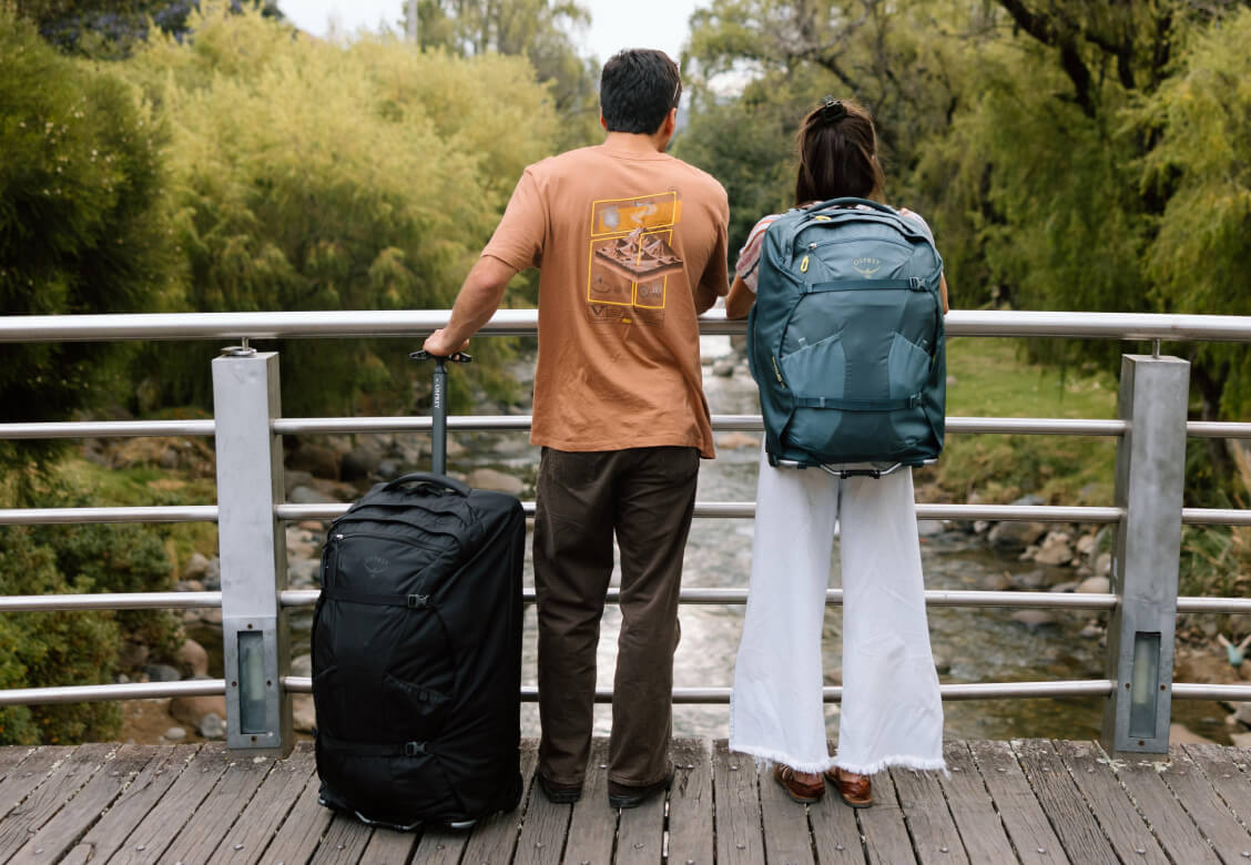 Two travelers with wheeled bag and Osprey backpack overlooking riverside walkway
