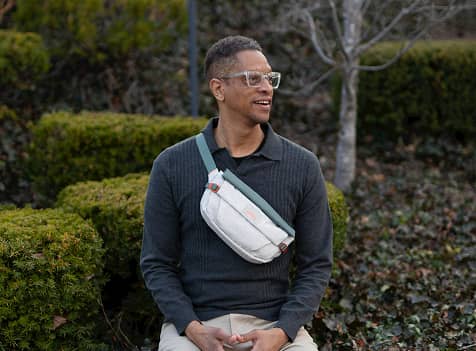 Person wearing a white Osprey sling bag across the chest while walking outdoors in a park setting.