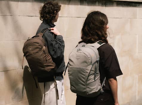 Two people wearing Osprey daypacks while walking in a city environment.