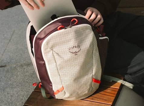 Close-up of an Osprey backpack with a laptop being placed inside a padded compartment.