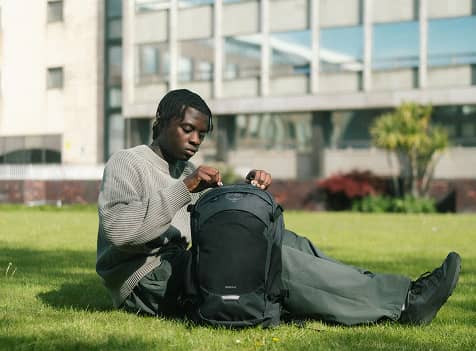 Person organizing gear in an Osprey backpack while sitting on a grassy lawn.