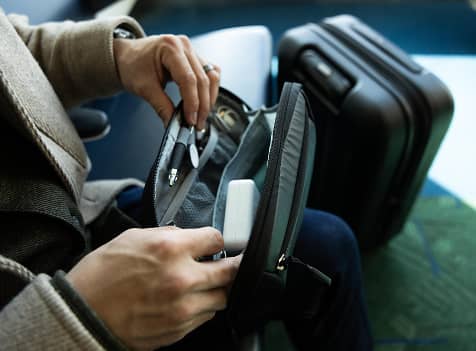 Close-up of a traveler organizing essentials in an Osprey backpack alongside rolling luggage.