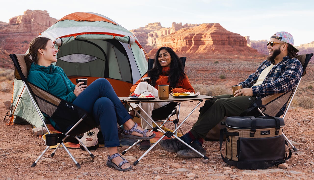 Three people lounge at a scenic desert campsite outfitted with an assortment of Campcore products.