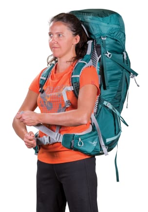 En kvinne i en oransje T-skjorte med trykk som har en blågrønn backpacker-ryggsekk på ryggen, strammer hoftebeltets justeringsstropp i nylon.