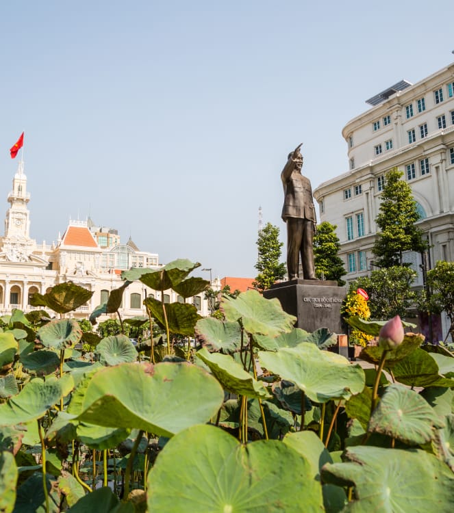 Lotusblader og -knopper i forgrunnen og Ho Chi Minh-statuen foran rådhuset i Ho Chin Minh-byen i Vietnam.