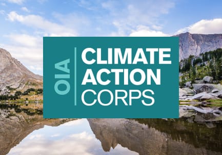 Den blågrønne og hvite logoen til OIA Climate Action Corps på et bakgrunnsbilde av et skog- og granittfjellområde med et speilblankt fjellvann og blå himmel.