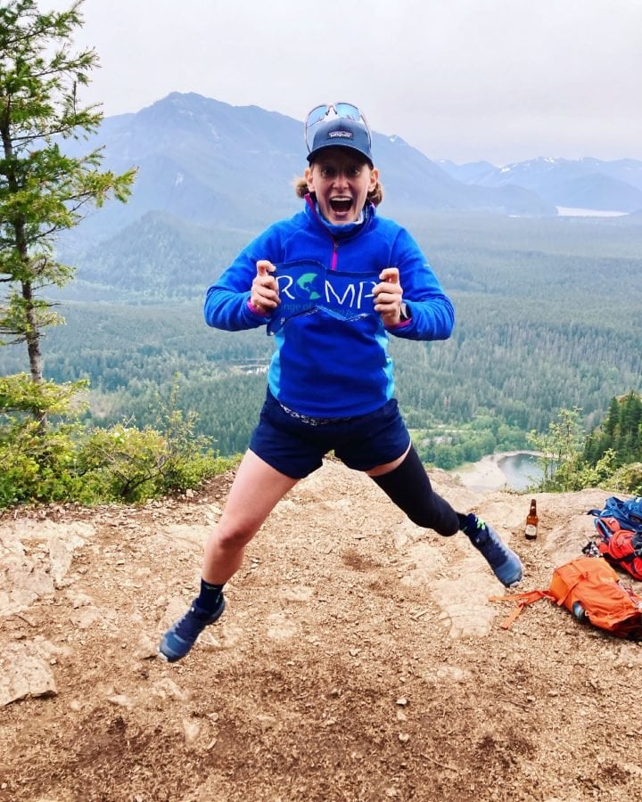 Nicole Ver Kuilen doing a celebratory jump atop a mountain wearing ROMP shirt.