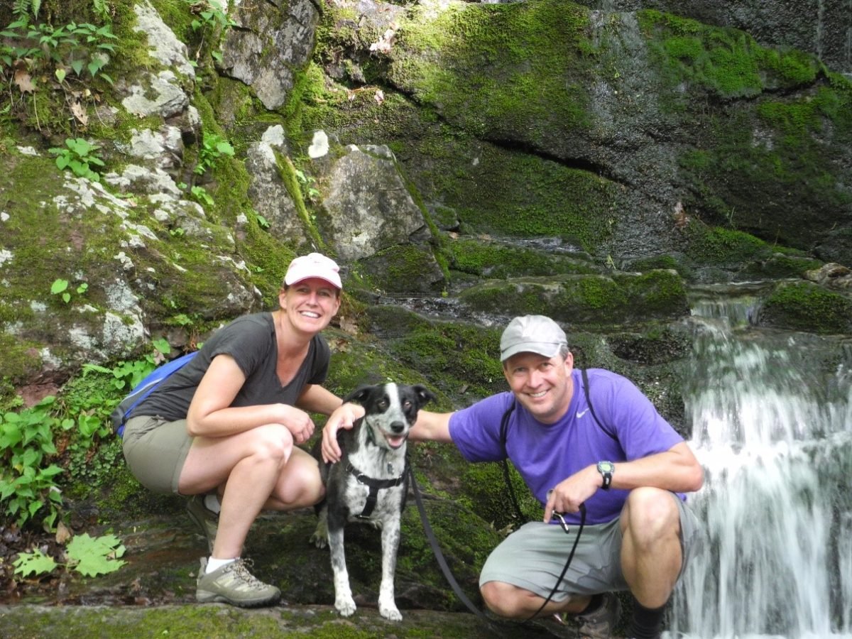 A man and a woman crouching down next to their dog beside a waterfall
