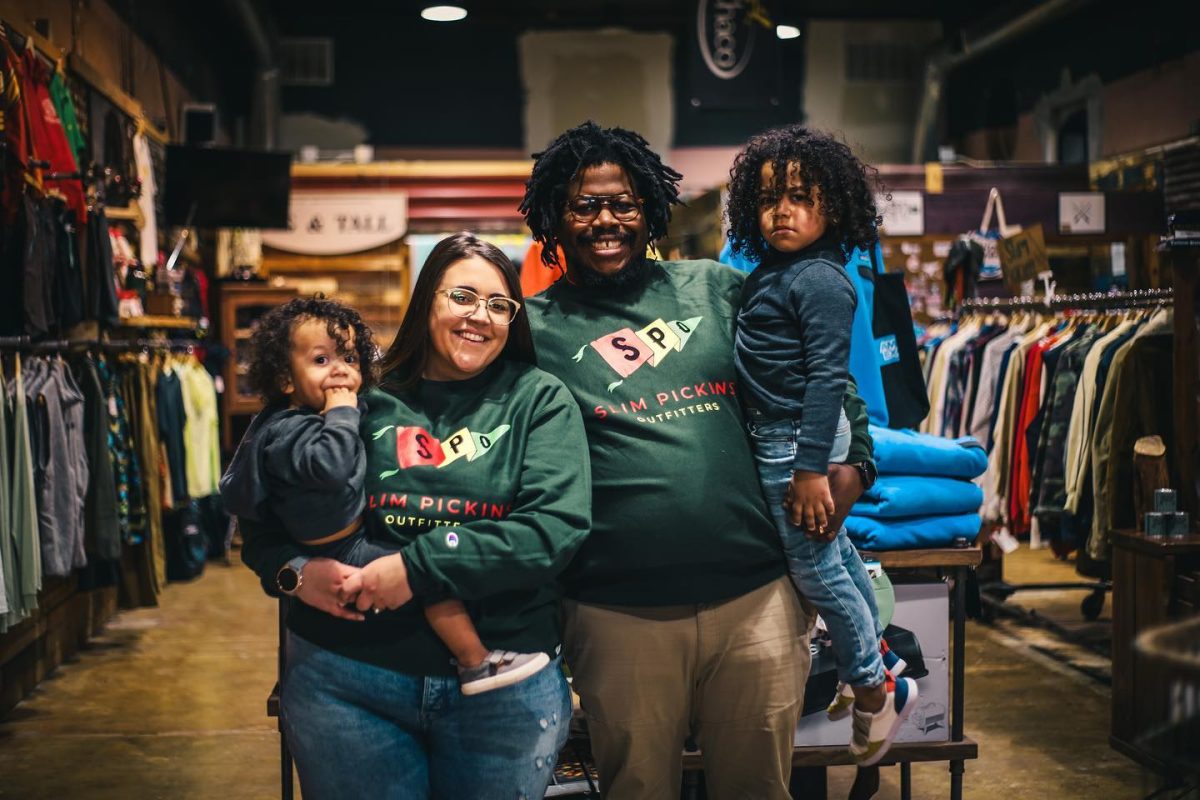 A man and a woman holding their two kids, wearing matching outfits inside their store