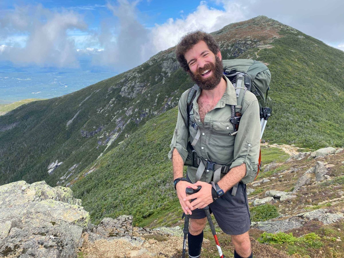A man posing along the Appalachian Trail, with grassy mountains in the background