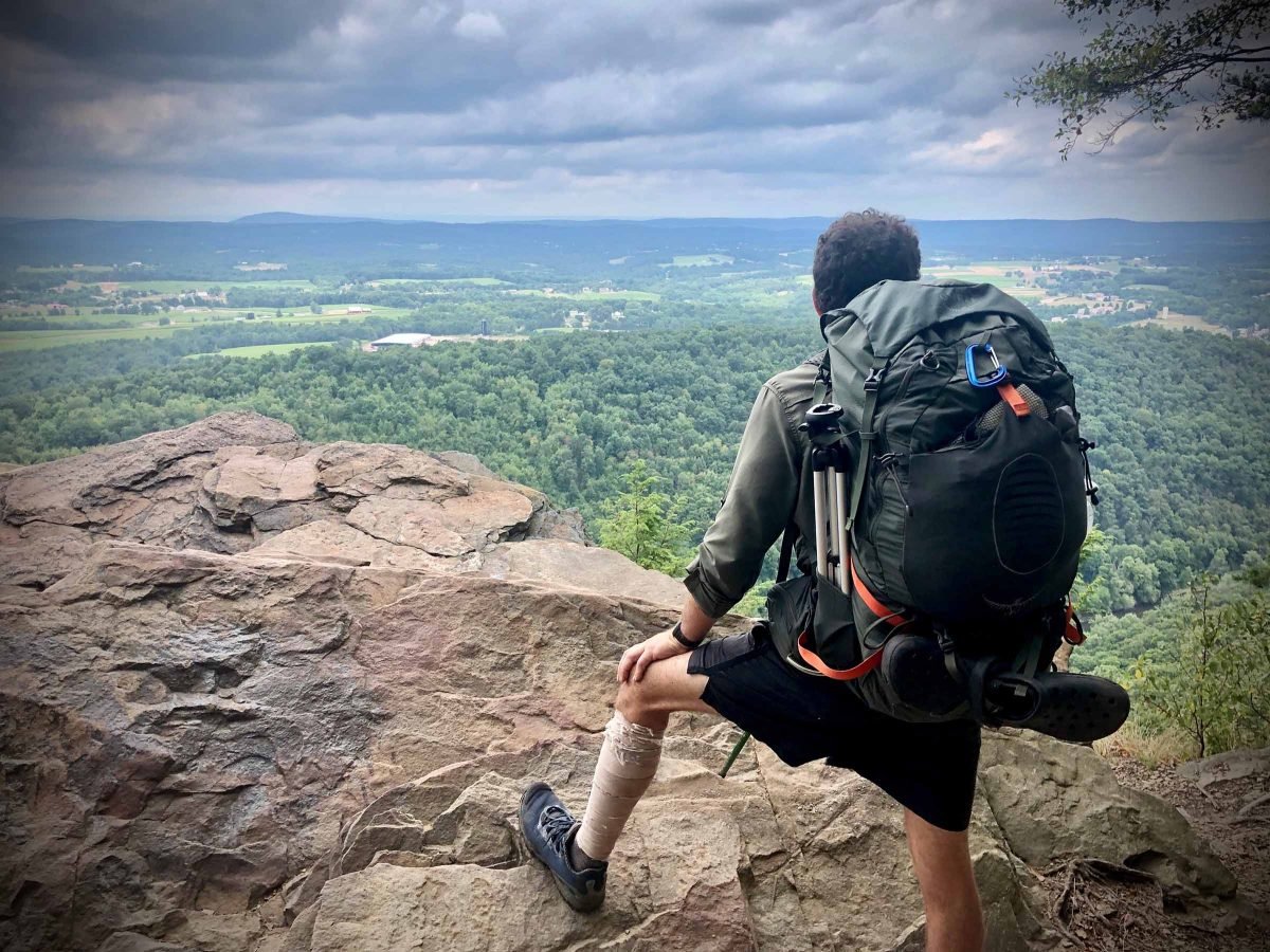 A man taking in the view of the landscape in the distance while atop a mountain overlook