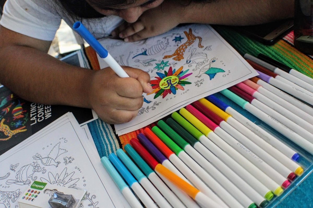 A close up of a child coloring a page, with markers next to them