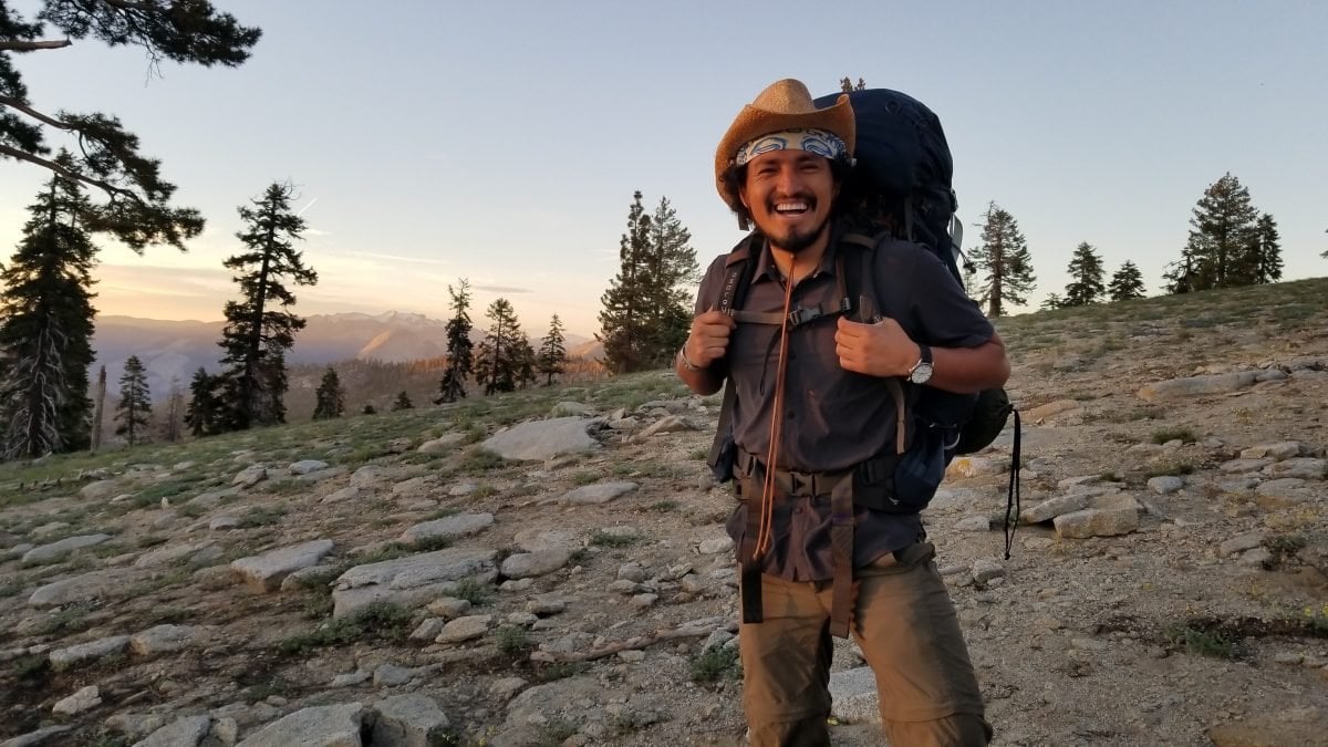 A man standing with his backpacking gear along a rocky backdrop