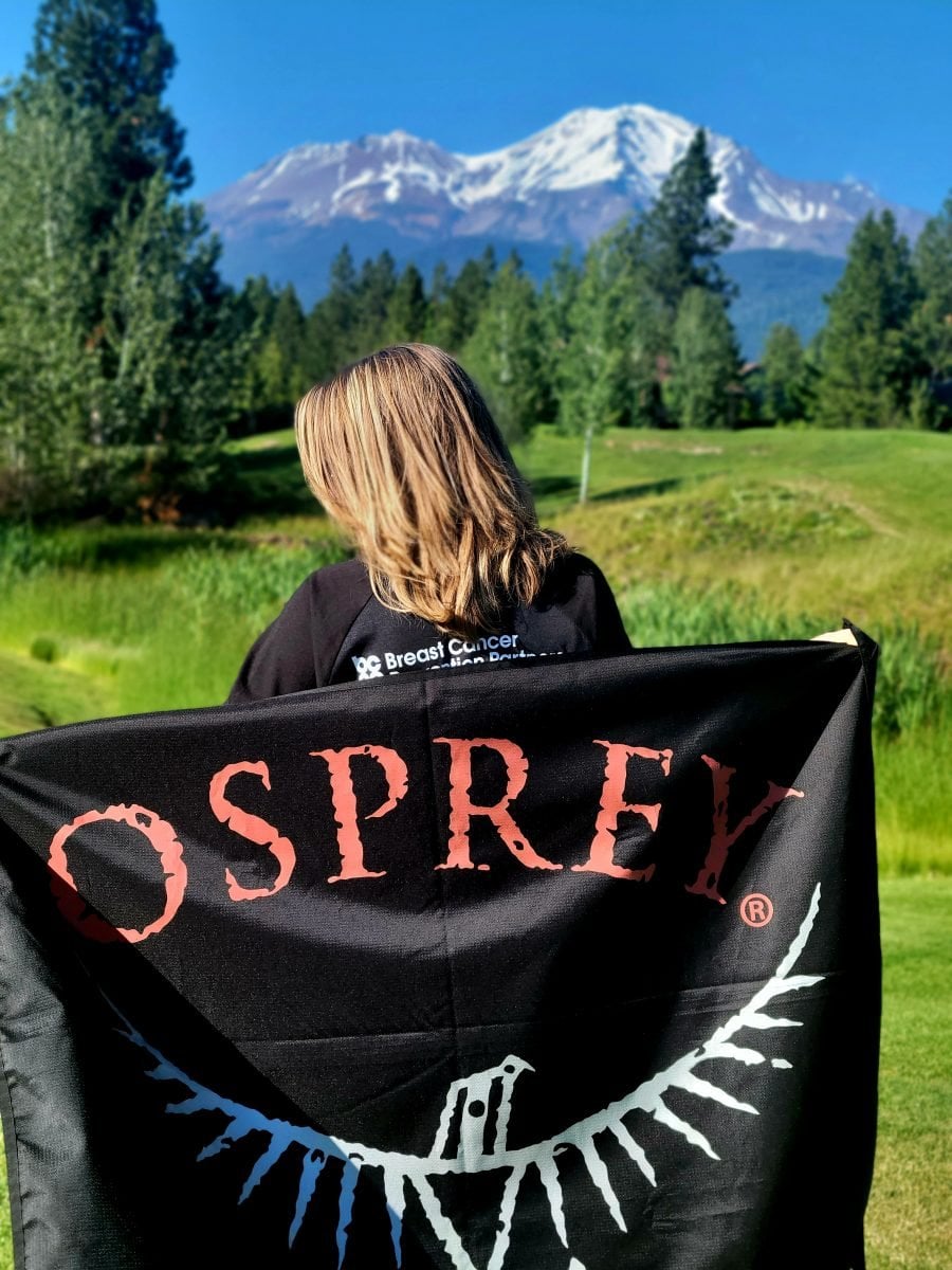 A woman holding an Osprey flag with Mount Shasta in the distance