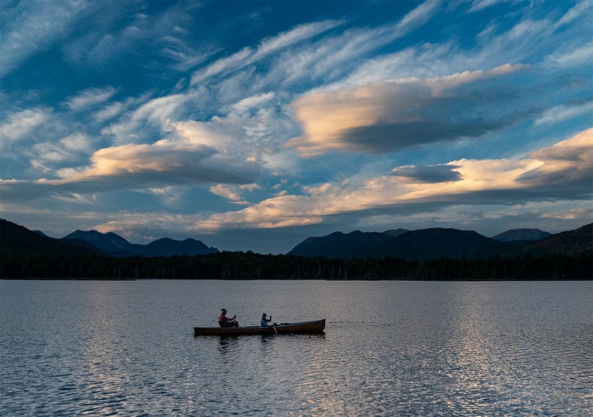 Two people in a kayak in a lake at dusk, with mountains in the distance