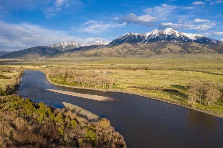 A sweeping view of a river through an open landscape, with a snow-covered mountain range in the distance