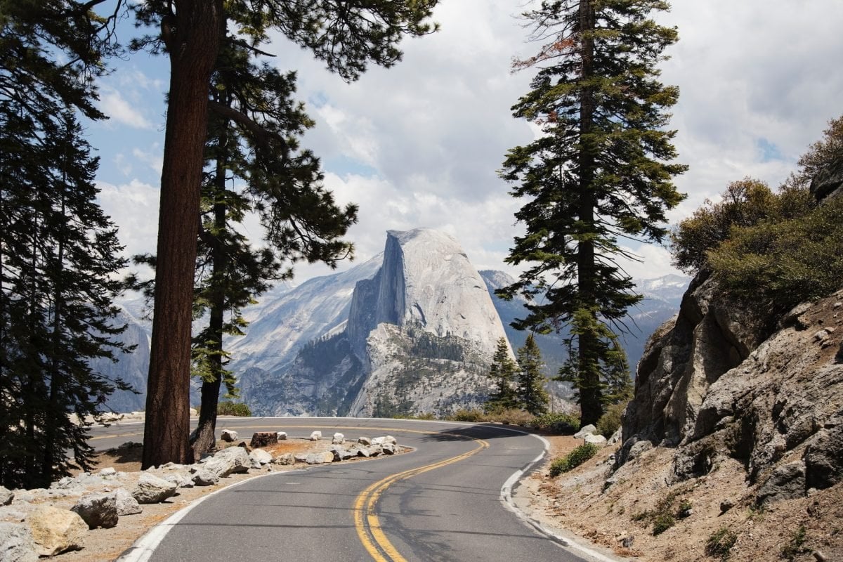 A view of a mountain range with a windy road in the foreground, and trees on either side.