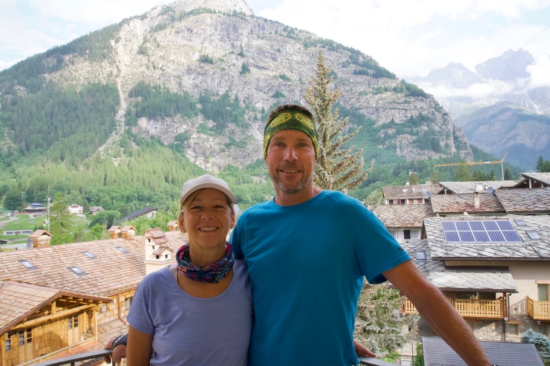 A man and woman posing with housing structures and a mountain in the background