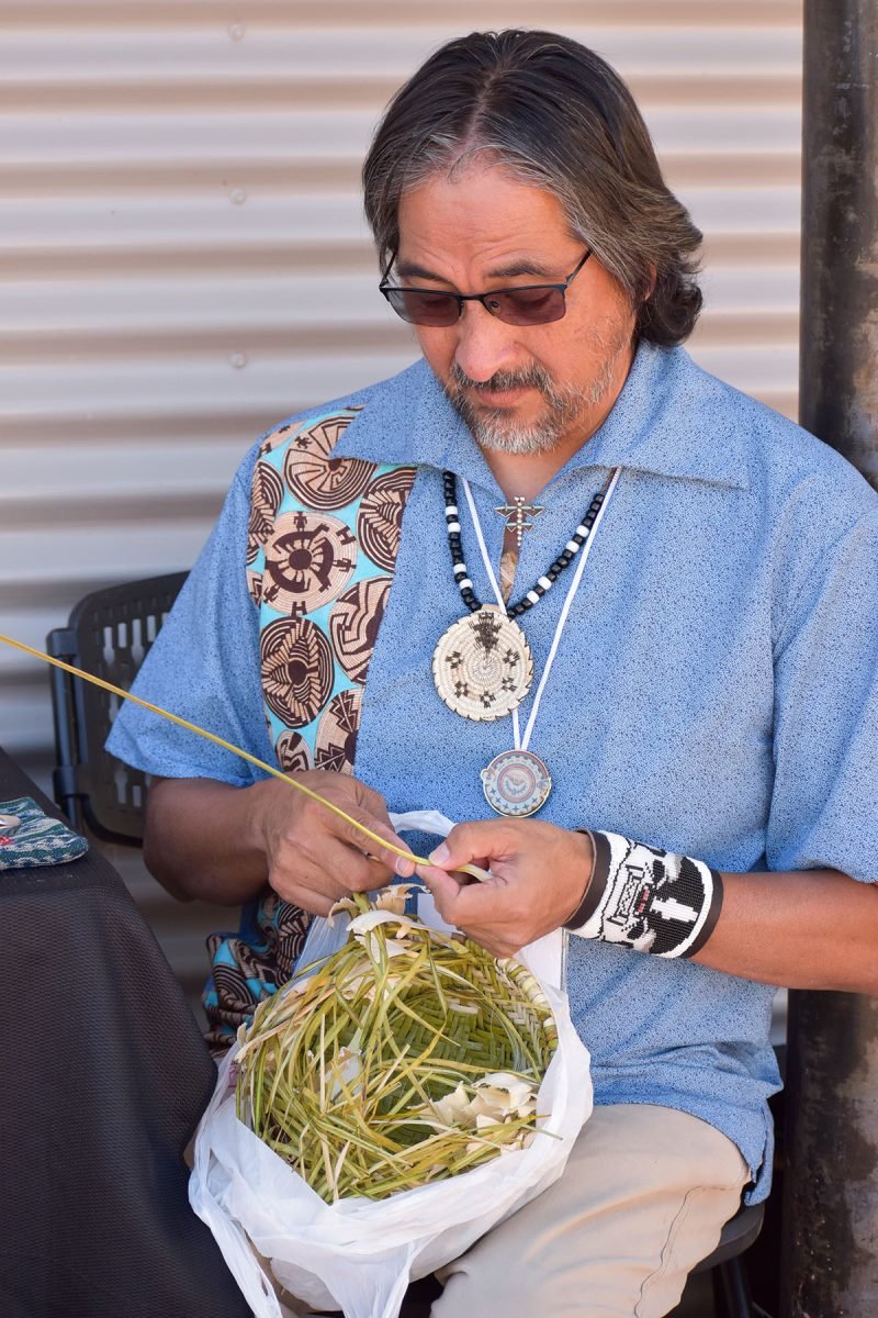 A man weaving in his lap with native plants