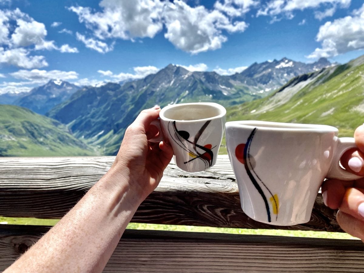 Two hands extended, holding small, decorative coffee mugs