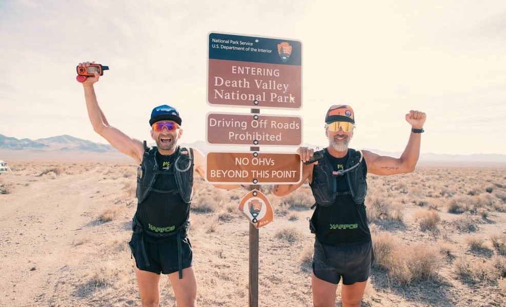 Two men standing near the Death Valley National Monument signage that reads 
