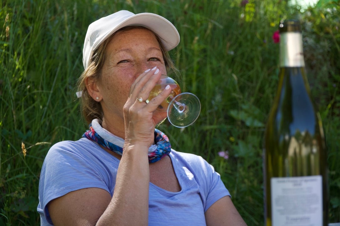 A woman drinking a glass of wine, a bottle in the foreground