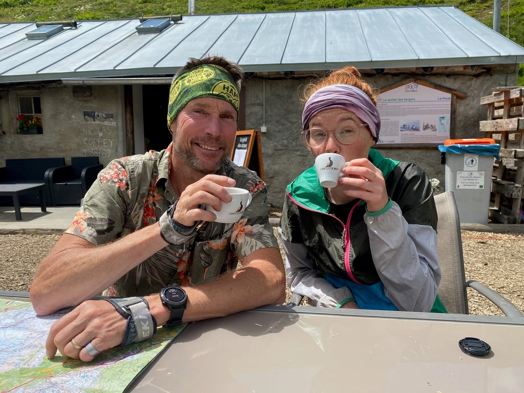 A man and woman sitting outside at a table, holding and sipping coffee cups