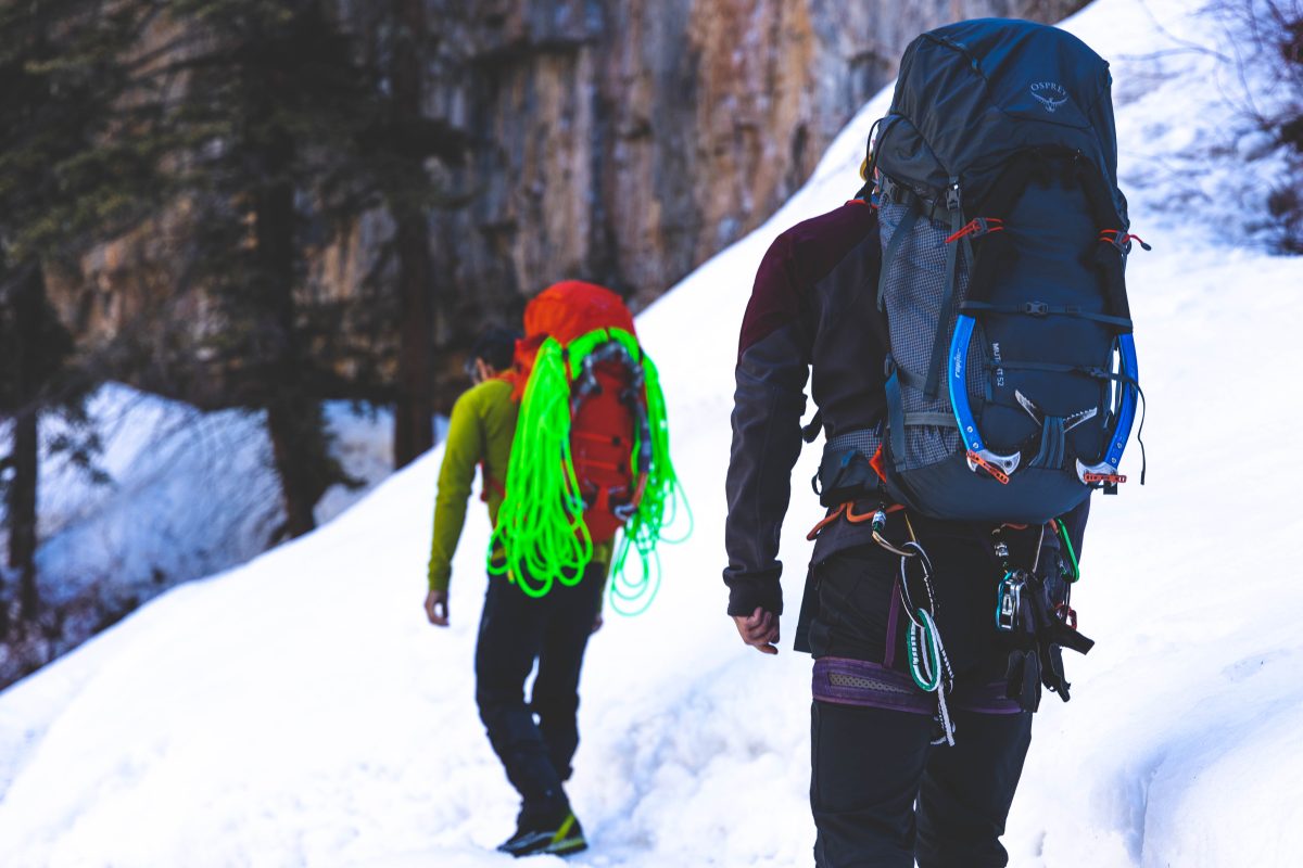 Two mountaineers trekking along a snowy trail, loaded with gear