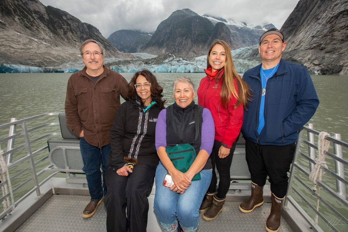 Five people posing together on a boat with a river and mountains in the background