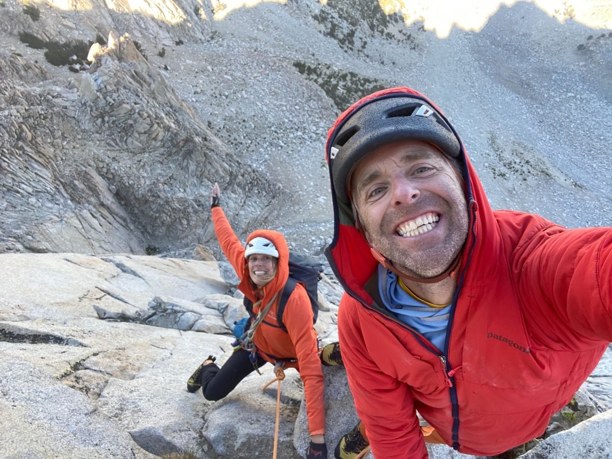 A man and woman rock climbing on a cliff face while posing and smiling