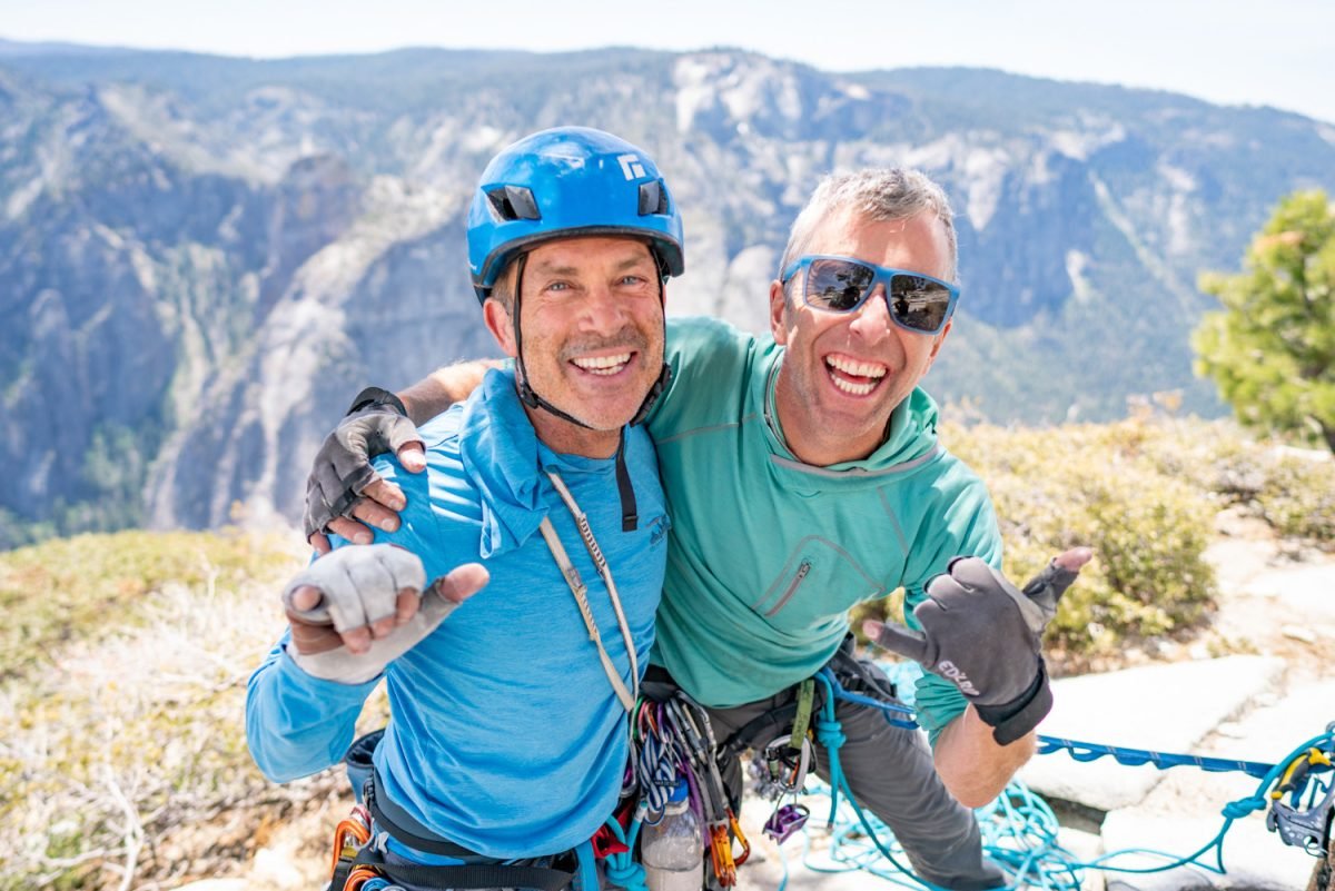 Two men geared up in rock climbing equipment smiling and posing together