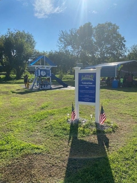 A sunny day at the park with a blue sign sharing information about the community