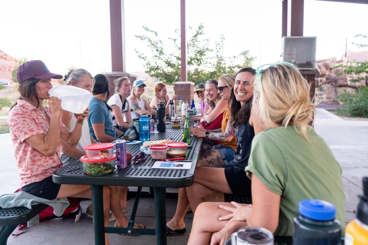 A group of women sitting around two park picnic tables chatting amongst each other