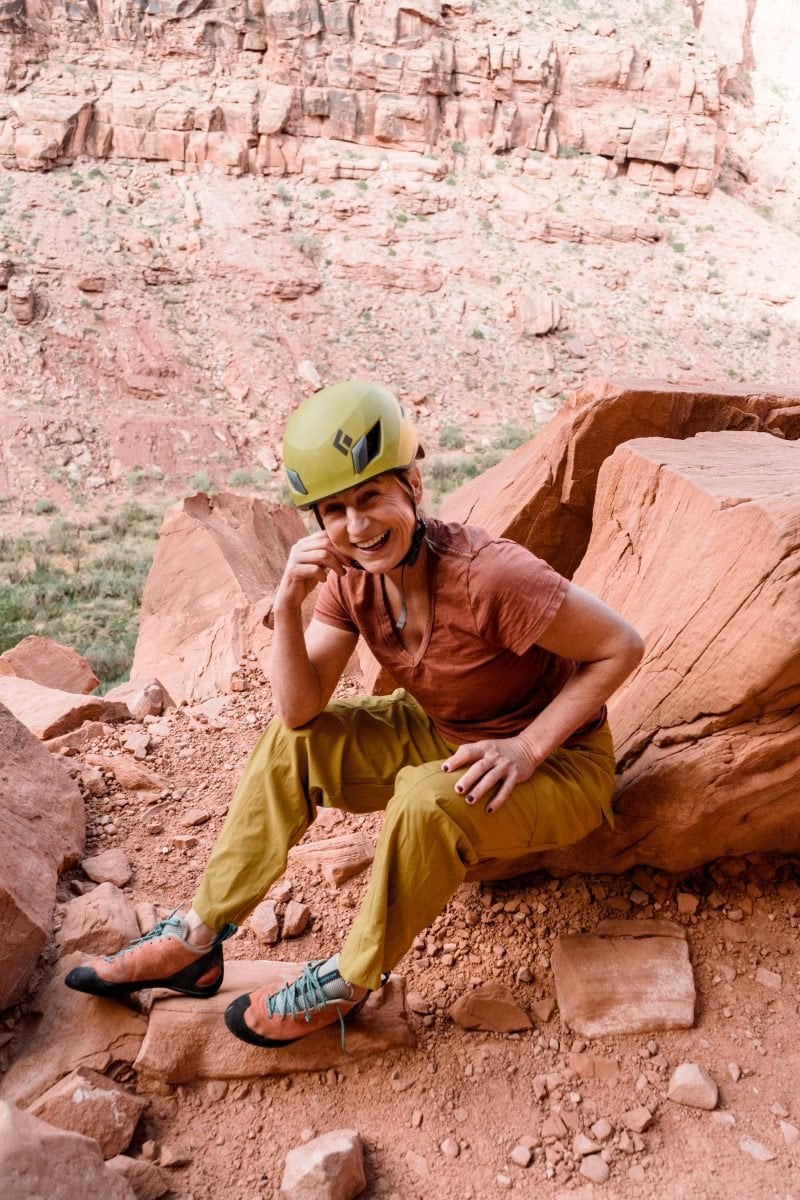 A woman sitting on a rock, wearing climbing gear, and smiling